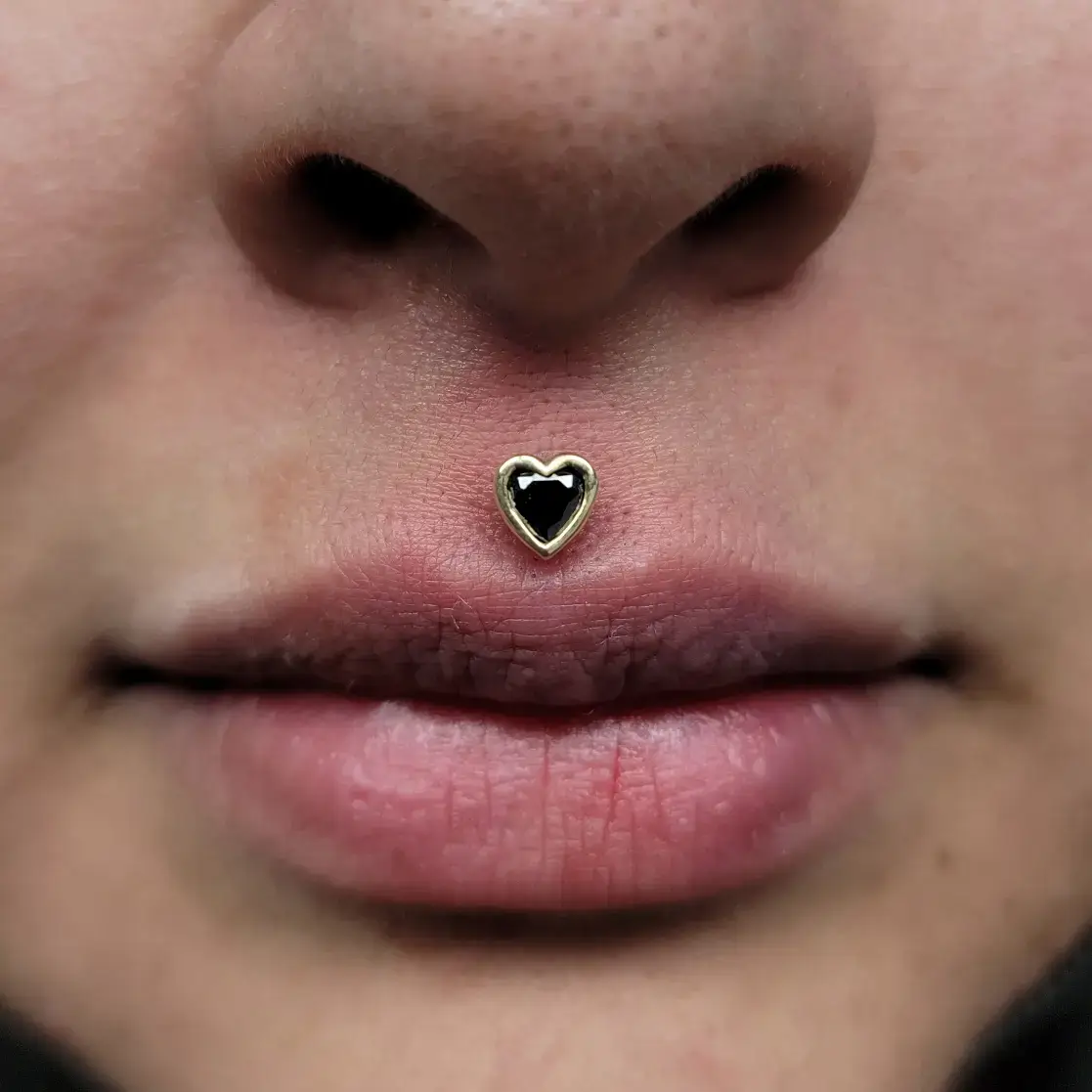 Philtrum piercing done with a BLM heart in yellow gold